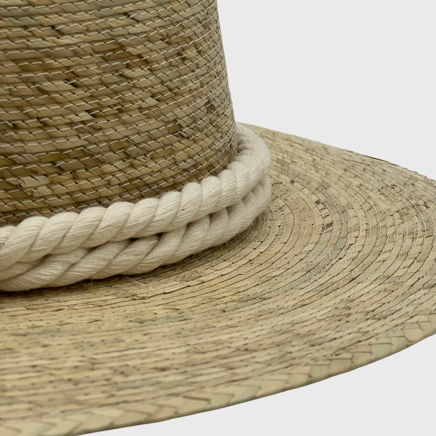 Close-up of a handwoven hat made of natural fibers, featuring a thick, white braided band around the base of the crown.