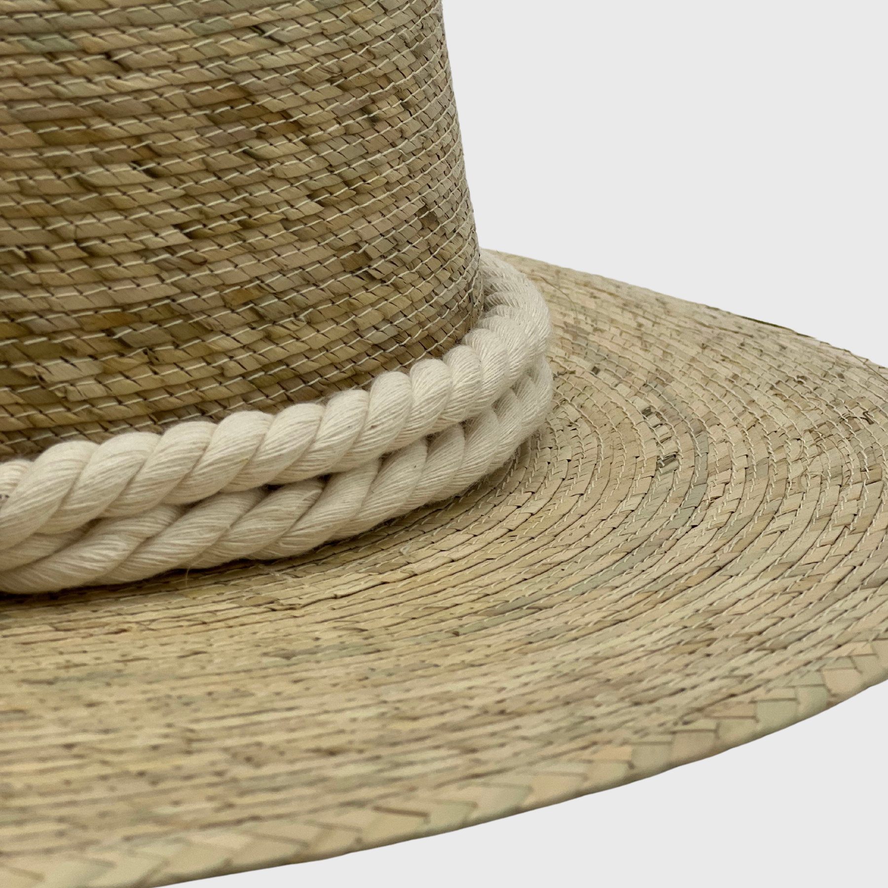 Close-up of a handwoven hat made of natural fibers, featuring a thick, white braided band around the base of the crown.