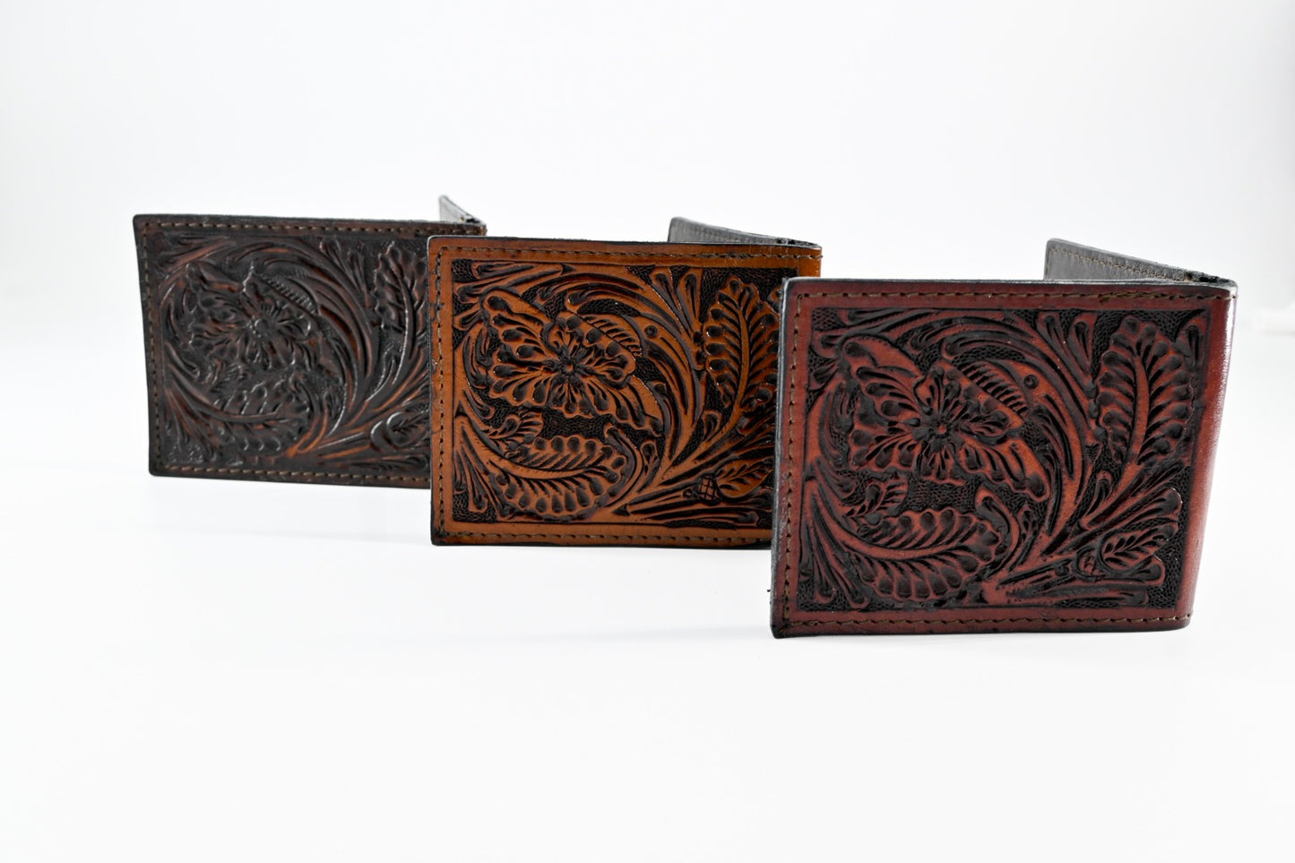 Three leather wallets with intricate floral carvings in a row, featuring black, caramel, and burgundy colors.