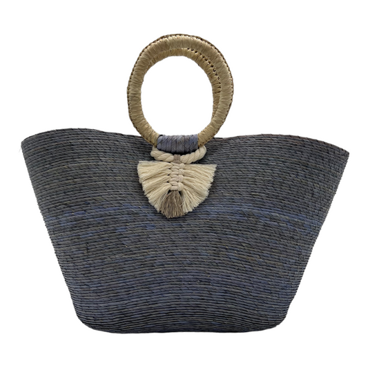 large woven tote bag in shades of gray and blue with a circular handle wrapped in natural fibers. The bag is adorned with a decorative tassel.