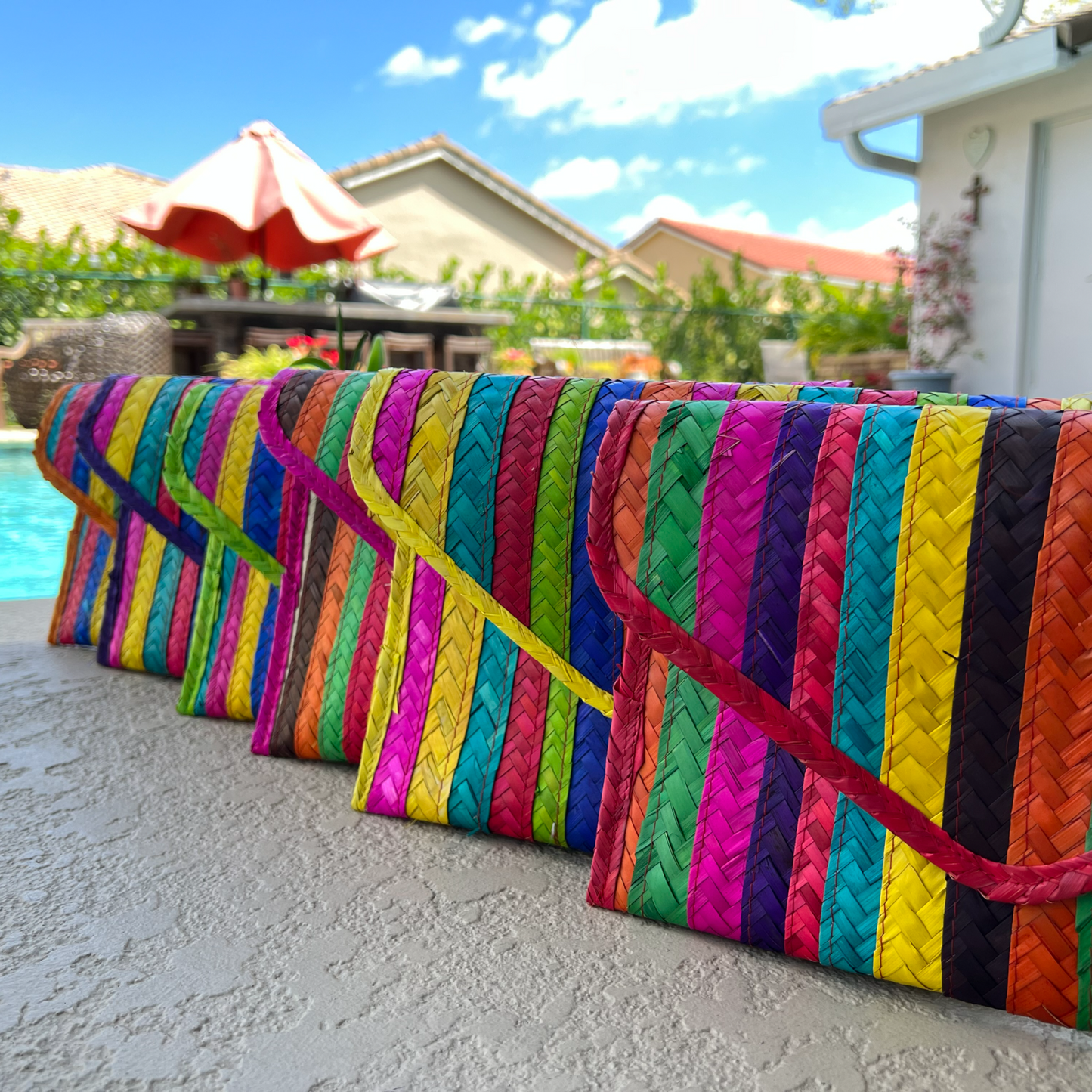 image shows a row of colorful, handcrafted woven clutches with diagonal stripes in various vibrant colors.