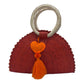 Red woven palm handbag with a circular handle wrapped in light material. The bag features a decorative heart with embroidery and a matching tassel on the front